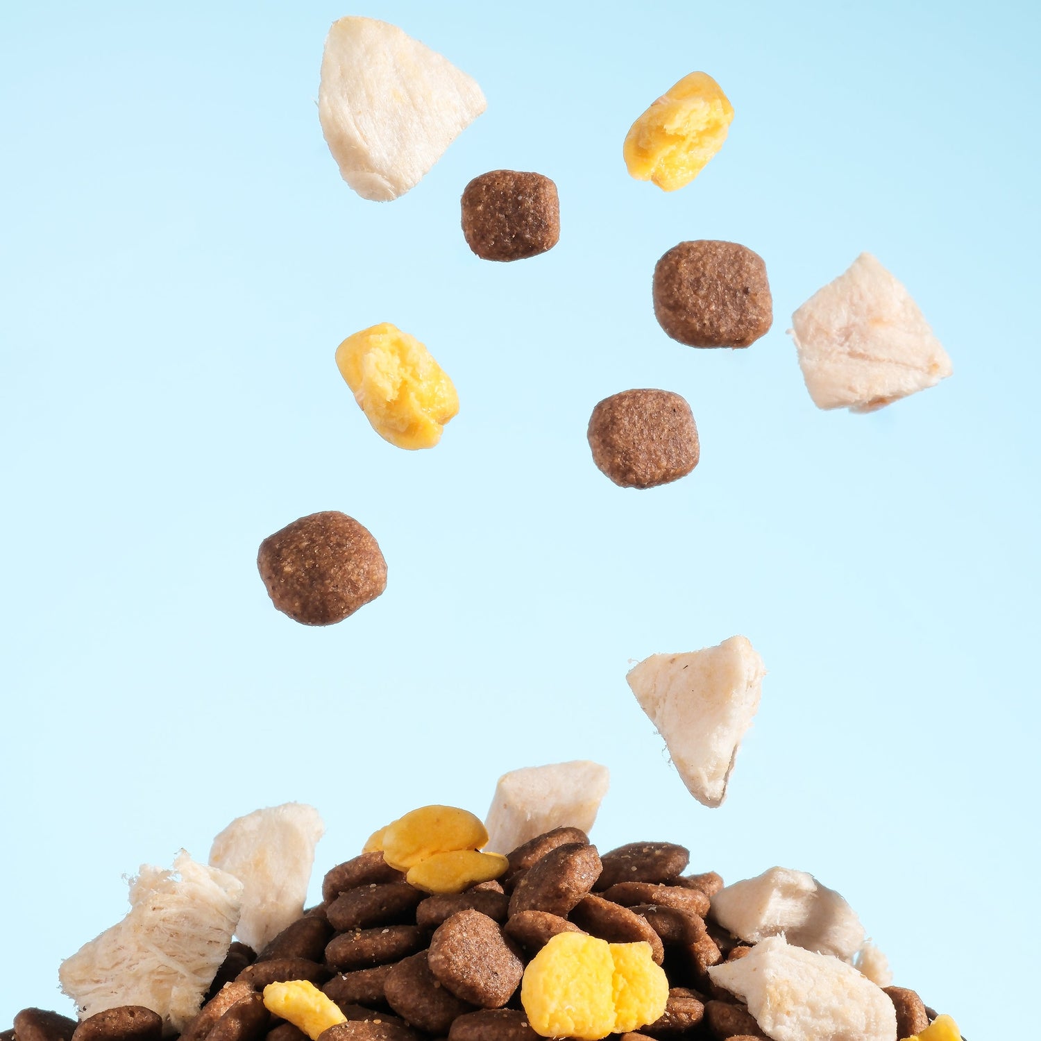 cat food pieces in various colors falling onto a pile of brown dog food against a light blue background.